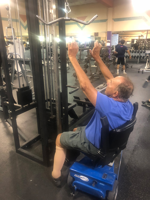 Man in wheelchair unable to reach bar on strength machine.